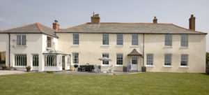 Exterior photo of Porthcothan House (a white Georgian Farmhouse with large windows)