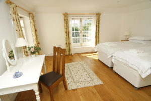 A light and spacious bedroom with twin beds , a dressing table and wooden floors
