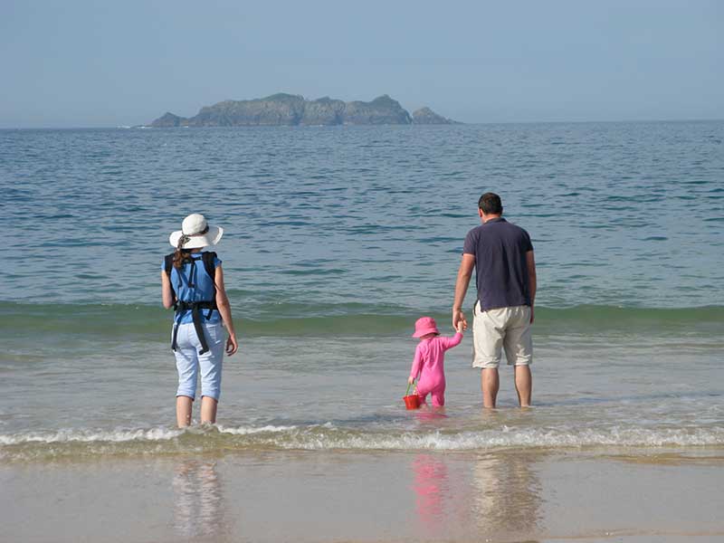 A family paddling in the shallow waves at a sandy beach with a rocky island in the distance