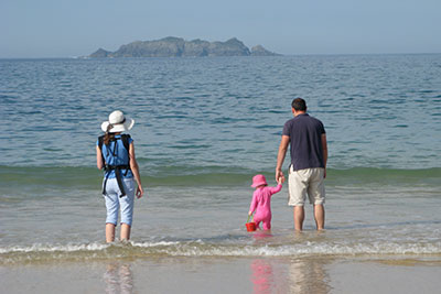 A family paddling in the shallow waves at a sandy beach with a rocky island in the distance