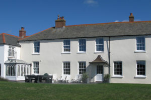 Exterior photo of Porthcothan House (a white Georgian Farmhouse with large windows)