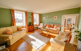 Light and spacious drawing room with wooden floors, green walls and several large sofas