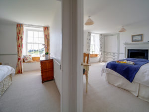 A view from a hallway looking into the doorways of two light and spacious bedrooms with beautiful bay window seats