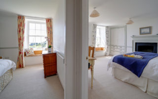 A view from a hallway looking into the doorways of two light and spacious bedrooms with beautiful bay window seats