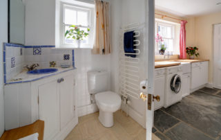 A light toilet room next to a spacious utility room with washing machine